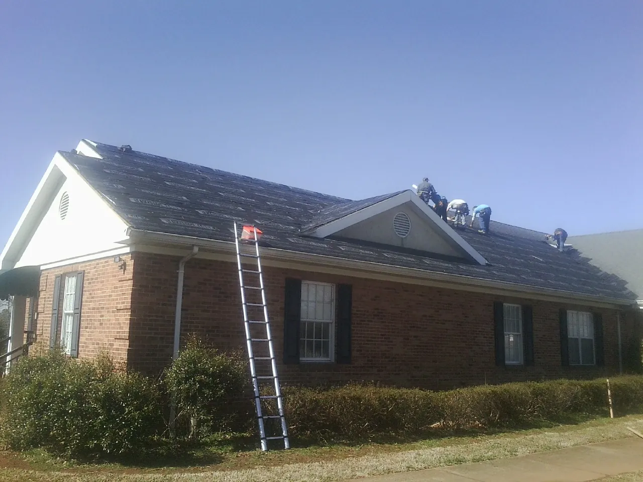 Crew tearing shingles off a brick ranch roof with a ladder set — Emergency Roof Repair work by our crew in Thornton