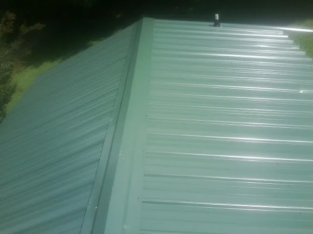 New green metal panels meeting at the ridge of a roof — Flat Roof Repair work by our crew in Thornton